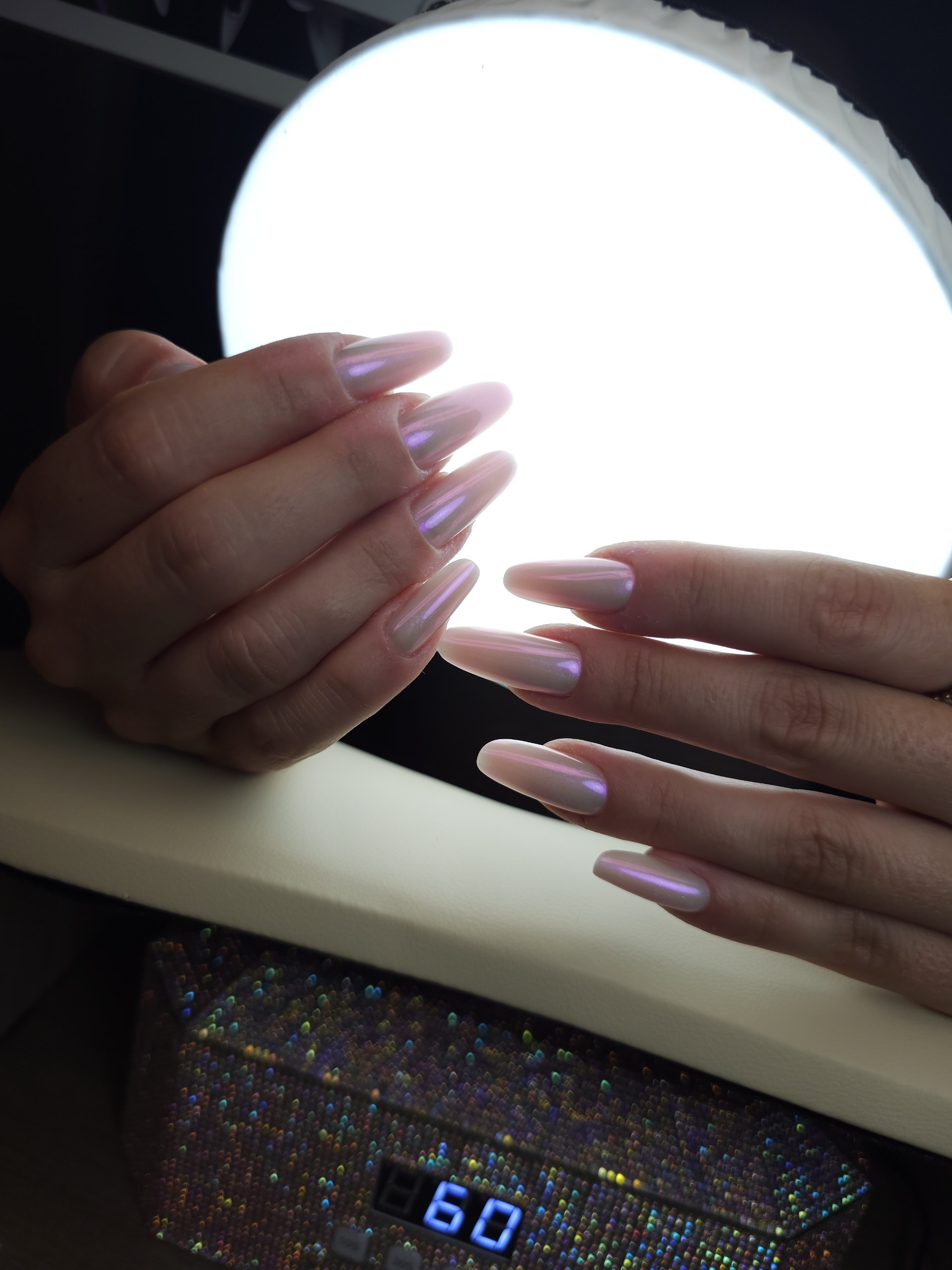 Hände mit perlmuttfarbener Chrome-Modellage vor der eingeschalteten UV-Lampe im Studio