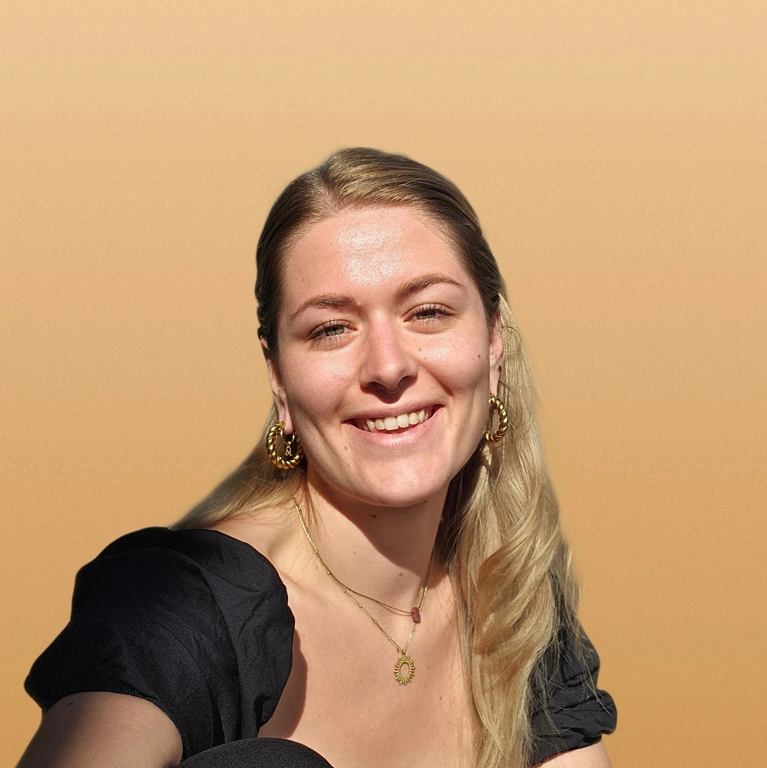 Nathalie, Inhaberin von Kallophia, lächelnd vor apricotfarbenem Hintergrund