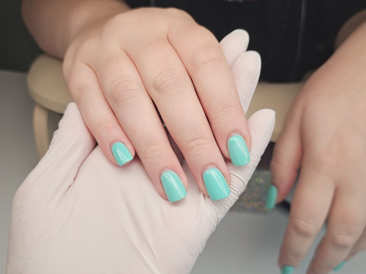 Hand mit türkiser Nagelmodellage vier Wochen nach dem Termin, nachgewachsener Nagel ohne Absatz